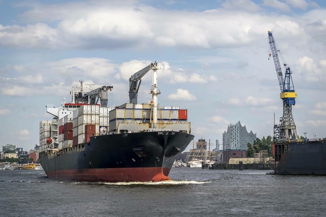 Ein Containerschiff im Hamburger Hafen mit Kränen und Stadtbild im Hintergrund