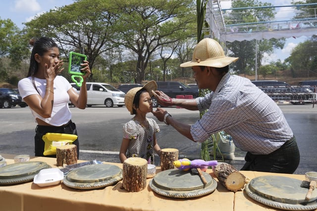 A man applies Thanakha, traditional make-up, on his child’s face as they take part in the first day of annual water festival also known as "Thingyan," in Naypyitaw, Myanmar, Sunday, April 13, 2025. (AP Photo/Aung Shine Oo)