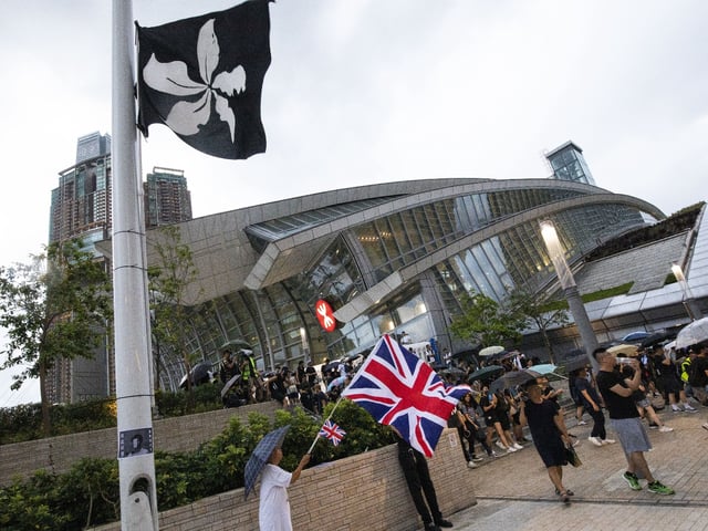 A demonstrator waves U.K. national flags, also known as the Union Jack, as an altered version of the Hong Kong Special Administrative Region (HKSAR) flag flies at half mast outside West Kowloon Station during a protest in Hong Kong, China, on Sunday, July 7, 2019. Hong Kong police arrested five people while dispersing a protest Sunday in one of the financial hub's busiest tourist districts, the latest demonstration triggered by a proposed law that would allow extraditions of criminals to mainland China for the first time. Photographer: Alex Hofford/Bloomberg via Getty Images