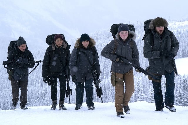 Fünf Menschen gehen mit Gewehren bewaffnet durch eine Schneelandschaft