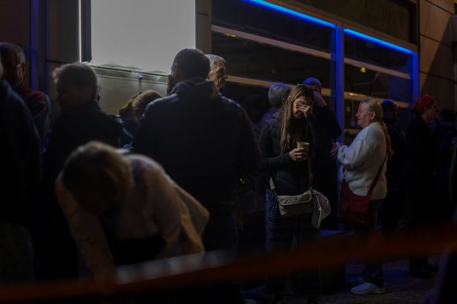 A woman reacts as customers of a nearby hotel stand on the street following a bomb blast outside the Hellenic Train offices, in Athens, Greece, April 11, 2025. REUTERS/Stelios Misinas
