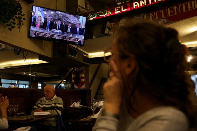 People watch Argentina's President Javier Milei give a speech as he addresses people on national TV, on the day Argentina's government reached an agreement with the International Monetary Fund board to approve a $20 billion loan deal in Buenos Aires, Argentina, April 11, 2025. REUTERS/Cristina Sille/File Photo