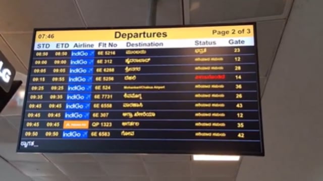A digital screen at the Bengaluru airport displaying flight numbers, destinations, status and gate numbers in Kannada and English only.