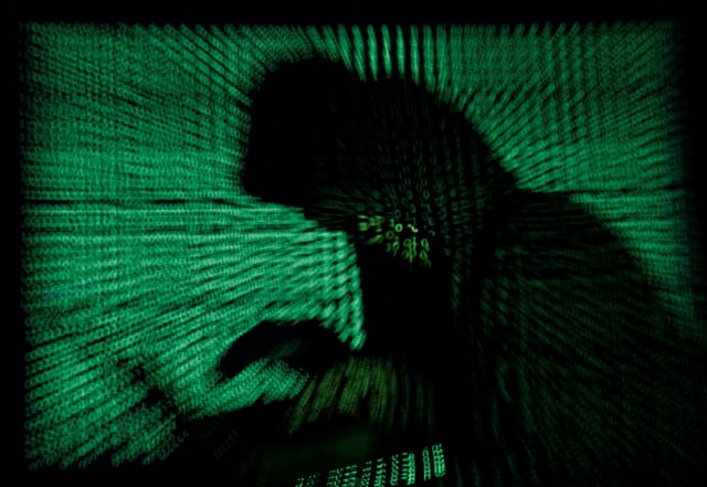 A hooded man holds a laptop computer as cyber code is projected on him in this illustration picture taken on May 13, 2017. REUTERS/Kacper Pempel/Illustration/File Photo