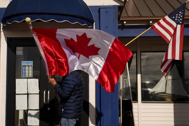 A worker at The Pier, in Point Robert, Washington, readjusts Canadian and American flags hanging outside the business, Monday, March 17, 2025.