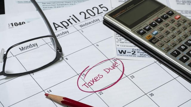 A calculator, pencil, glasses, and tax form sitting on top of an April 2025 calendar with the phrase "Taxes due" written on April 15.