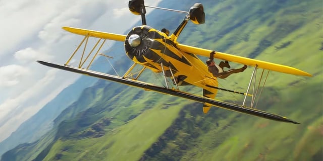 Tom Cruise as Ethan Hunt hanging on an upside down yellow byplane in Mission: Impossible 8.