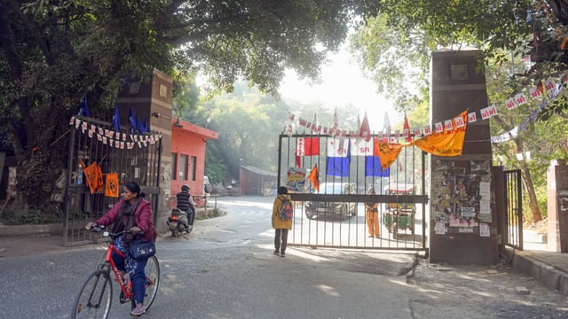 A woman passes on a cycle at the JNU gate. The notices warn that “any future complaints or violations will result in your immediate eviction from the hostel without prior notice”.