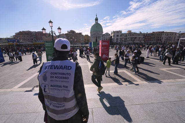 Stewards check tourists' QR codes outside the main train station in Venice, Italy, Friday, April 18, 2025, as the city for a second year is charging day-trippers an arrivals tax. (AP Photo/Antonio Calanni)