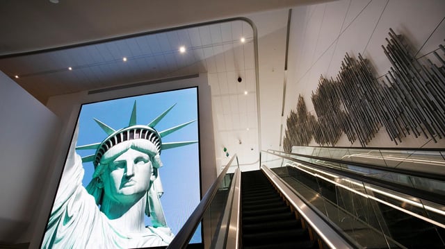 Ein Bildschirmbild der Freiheitsstatue begrüsst ankommende Reisende auf einer Rolltreppe des Flughafens LaGuardia, New York, USA