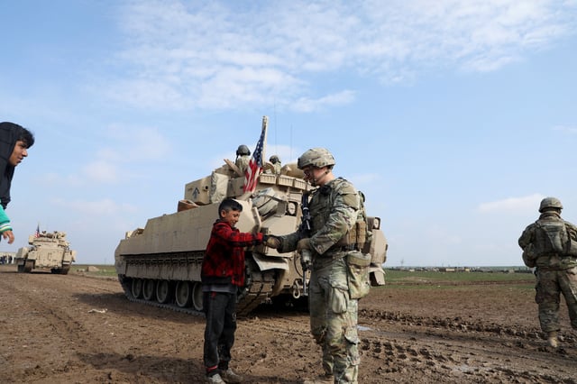 A soldier from the US-led coalition holds the hand of a boy during a joint U.S.- Kurdish-led Syrian Democratic Forces (SDF) patrol in the countryside of Qamishli in northeastern Syria February 8, 2024. REUTERS/Orhan Qereman/File Photo