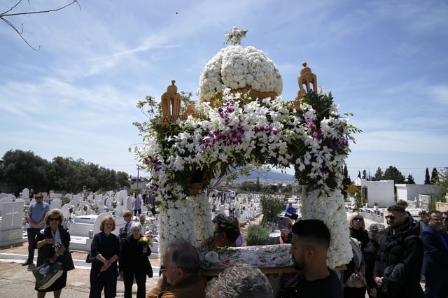 The procession of Jesus' funeral bier, known as the "Epitaph" in Greek, pass next to graves at a cemetery in Chalandri suburb, in northern Athens, Greece, Friday, April 18, 2025. (AP Photo/Thanassis Stavrakis)