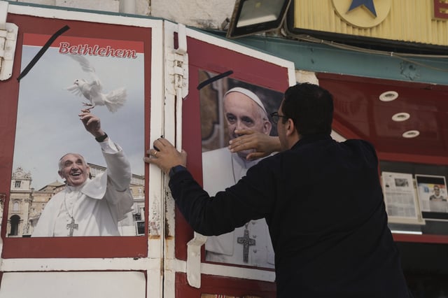 A shop owner cleans and places a black ribbon over a photo of the late Pope Francis after the news of his death at age 88, in Bethlehem, West Bank, on Monday, April 21, 2025.