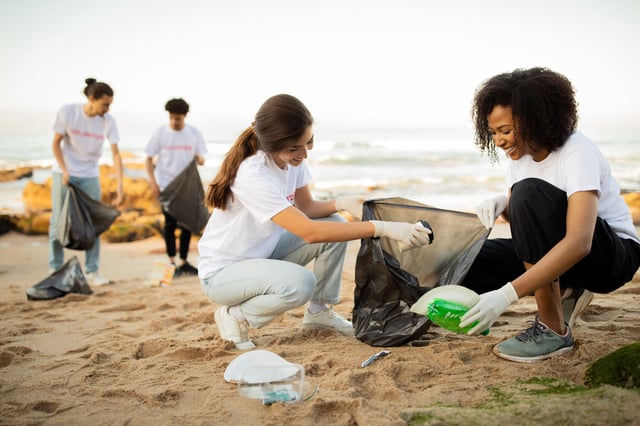 Young volunteers with globes and garbage bags clean up trash on a beach for Earth Day.