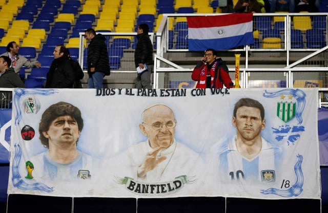 A Chile fan stands behind a banner depicting (L-R) retired Argentina soccer player Diego Maradona, Pope Francis and Argentina's Lionel Messi as he awaits the start of the Copa America 2015 semi-final soccer match between Argentina and Paraguay at Estadio Municipal Alcaldesa Ester Roa Rebolledo in Concepcion, Chile, June 30, 2015. REUTERS/Andres Stapff/File Photo