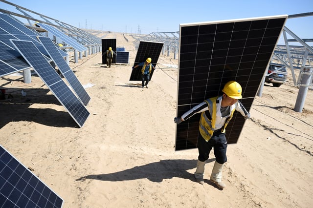 Des travailleurs transportent des panneaux solaires pour les installer dans une ferme solaire dans le désert, à Lingwu, dans la région autonome Hui de Ningxia, en Chine, le 14 avril 2025.