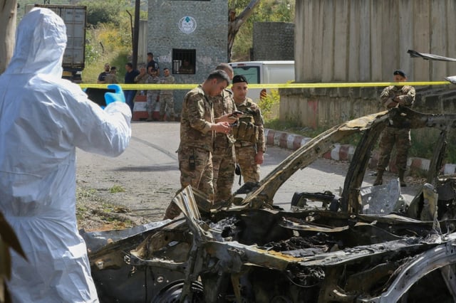 Security forces and forensic experts inspect a car targeted by an Israeli air strike near Damour