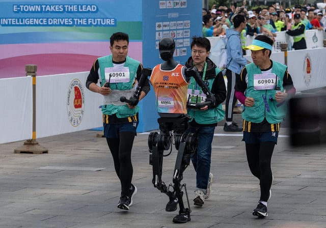 A Humanoid robot called Tiangong runs with support technicians in the Beijing E-Town Humanoid Robot Half-Marathon on April 19, 2025, in Beijing, China.