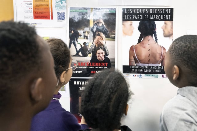 Des élèves de primaire regardent des affiches expliquant qu'il ne faut pas se taire face au harcèlement. 