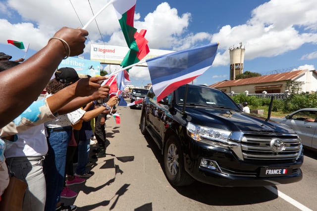 Residents wave flags at French President Emmanuel Macron upon his arrival in Antananarivo, Madagascar, Wednesday, April 23, 2025. (AP Photo/Alexander Joe)
