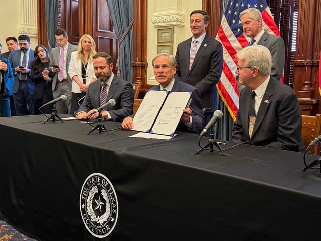 Texas Gov. Greg Abbott, center, holds a newly signed bill creating the Texas Regulatory Efficiency Office during a ceremony inside the state Capitol on Wednesday, April 23, 2025, in Austin, Texas. (AP Photo/Nadia Lathan)