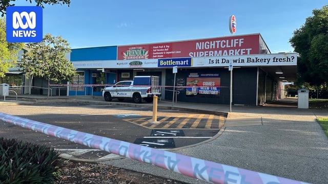 A small grocery store taped off with police tape and a police vehicle parked in front.