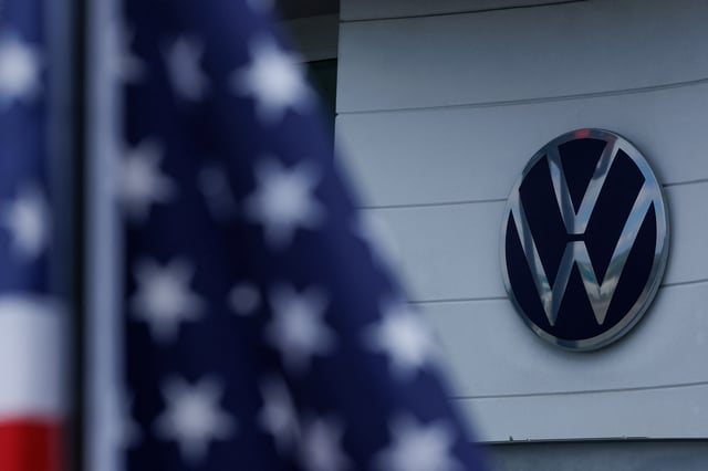 The Volkswagen logo is shown next to an American flag at a Volkswagen dealership in Irvine, California, U.S., March 27, 2025.  REUTERS/Mike Blake/ File Photo