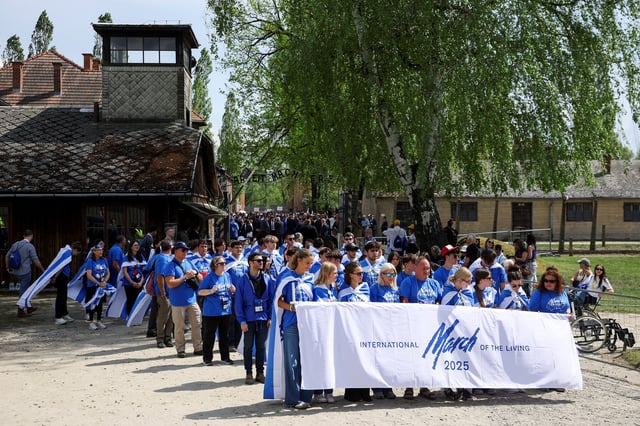 People hold a banner near the "Arbeit macht frei" (Work sets you free) gate, on the day of the annual International "March of the Living" through the grounds of the former Auschwitz death camp, to pay tribute to the millions of Jews murdered by the Nazis during World War Two, in Oswiecim, Poland, April 24, 2025. REUTERS/Kacper Pempel