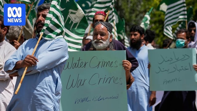 A man holds a sign at a protest that reads, "Water crimes, war crimes" among a sea of green and white flags