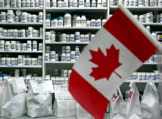 A Canadian flag -- a flag with two red stripes on either side and a red maple leaf against a white background -- in front of an array of medication bottles.