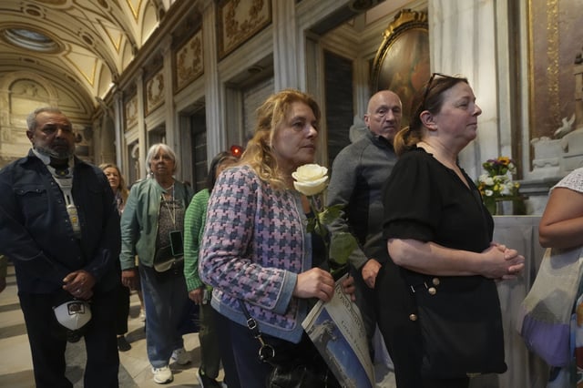 A woman holds a white rose as she waits in line to pay her respects to the tomb of Pope Francis inside St. Mary Major Basilica in Rome, Sunday, April 27, 2025. (AP Photo/Alessandra Tarantino)