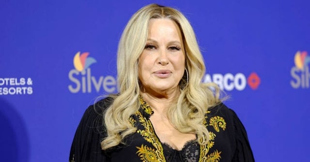 Person with long, wavy hair and a confident expression at a public event, wearing elegant attire