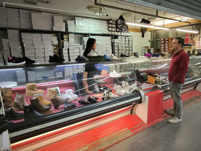 Una mujer atiende a un cliente en una zapatería que tuvo que ser trasladada al mercado de Benetússer