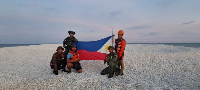 Philippine officers unfurl their national flag on a sandbar in Sandy Cay on April 27, 2025.