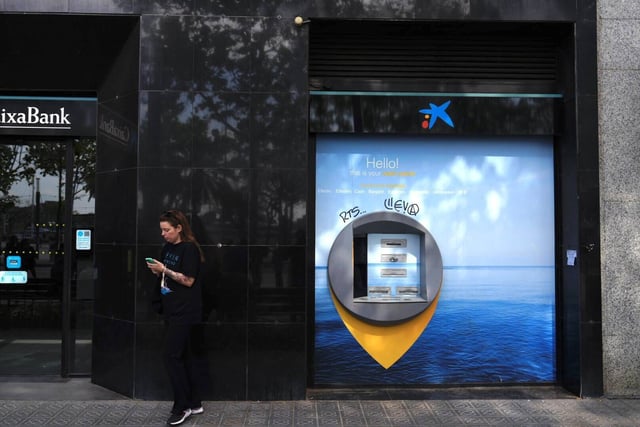 Una mujer consulta su móvil junto a un cajero automático este lunes en Barcelona.