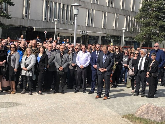 Attendees at the local Day of Mourning ceremonies Monday at Laurentian University observe a moment of silence as flags in the courtyard were lowered to half staff.