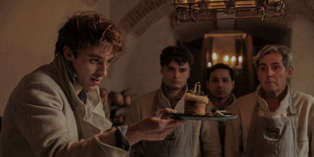 Antonin (Benjamin Voisin) holding up a pastry on a plate in Carême
