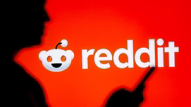 A woman looking at a smartphone with a Reddit logo displayed in the background
