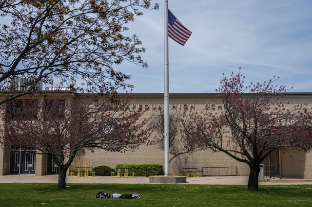 A person lies on the grass in front of Massapequa High School, in Massapequa, N.Y., Friday, April 25, 2025. (AP Photo/Julia Demaree Nikhinson)