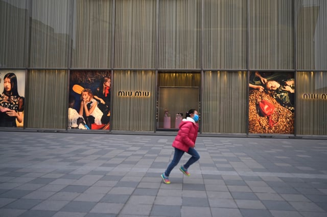 A child wearing a face mask runs past a store of Miu Miu in Beijing, China February 20, 2020. REUTERS/Tingshu Wang/File Photo