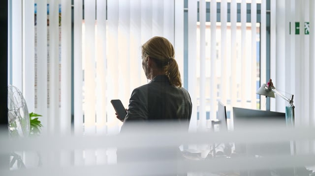Eine Frau steht in einem Bürozimmer am Fenster und telefoniert über ein Headset