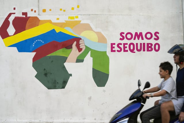 FILE - A youth drives a motorcycle in front of a mural of a map of Venezuela with the Essequibo territory, a swath of land administered and controlled by Guyana but claimed by Venezuela, in the 23 de Enero neighborhood of Caracas, Venezuela, Dec. 11, 2023. (AP Photo/Matias Delacroix, File)