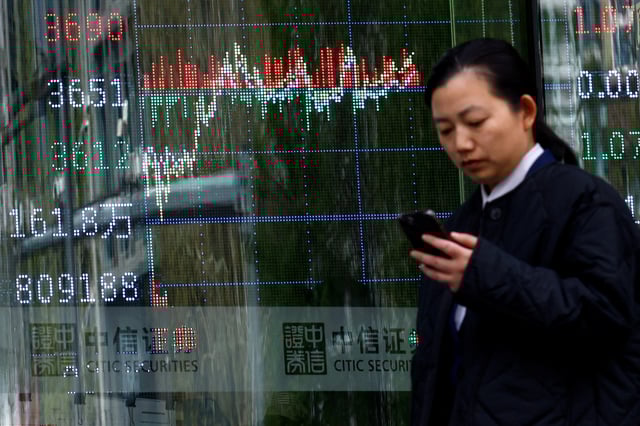A woman walks past a brokerage house with a display board showing the stock index information, in Beijing, China April 9, 2025. REUTERS/Tingshu Wang/File Photo