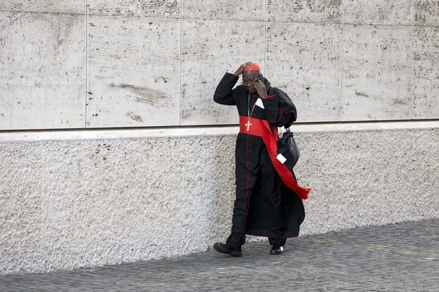 Cardinal Philippe Ouedraogo holds his skull cap as he arrives for the afternoon session of the Synod of bishops, at the Vatican, Thursday, Oct. 22, 2015.