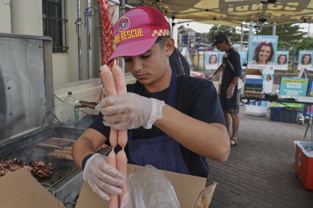 A volunteer prepares to cook sausages on a BBQ outside a polling booth at Sydney's Bondi Beach, Saturday, May 3, 2025. (AP Photo/Mark Baker)