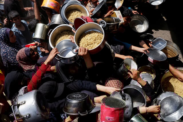 Palestinians gather as they receive food cooked by a charity kitchen, in Khan Younis, southern Gaza Strip, April 29, 2025. REUTERS/Hatem Khaled/File Photo