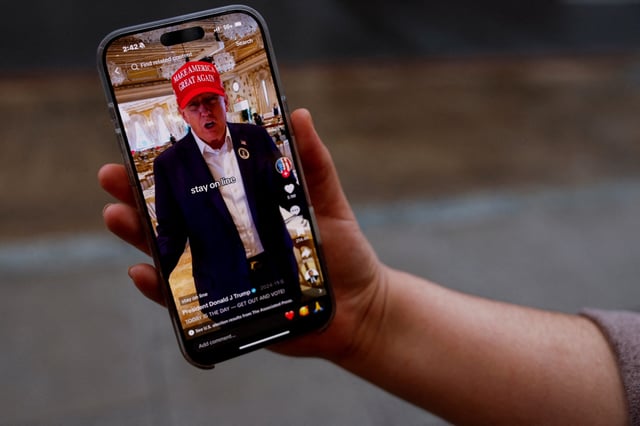 A woman poses with her smartphone displaying the @realdonaldtrump TikTok page, in Washington, U.S. January 19, 2025. REUTERS/Shannon Stapleton/File Photo