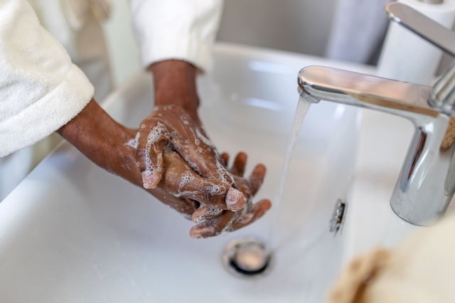 Close-up of a person lathering hands with soap and water over a bathroom sink, promoting hygiene and health.