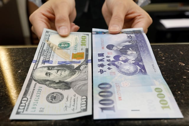 A teller poses with U.S. $100 and New Taiwan dollar (TWD) $1000 banknotes at a bank in Taipei, Taiwan February 23, 2017. Picture taken February 23, 2017. REUTERS/Tyrone Siu