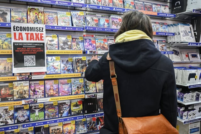 Customers browse products at a Game Stop store next to a sign advertising 'save the tax' in Montreal on December 14, 2024. THE CANADIAN PRESS/Graham Hughes
